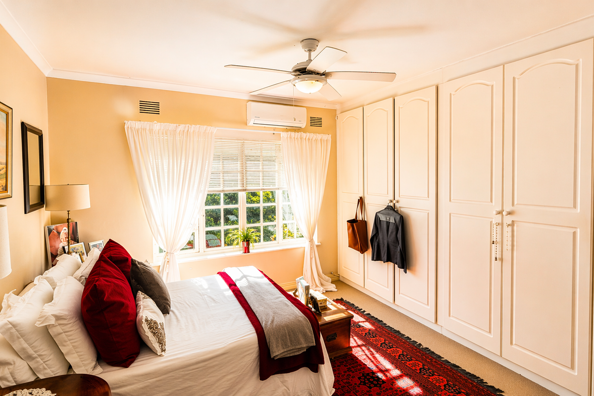 A well-maintained bedroom featuring extensive built-in cabinetry, a ceiling fan, and a wall-mounted air conditioning unit.