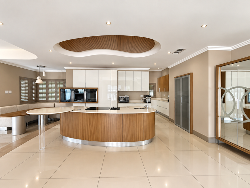 Modern kitchen featuring a curved island with integrated cooktop, high-gloss cabinetry, built-in ovens, and a unique recessed ceiling design with ambient lighting.