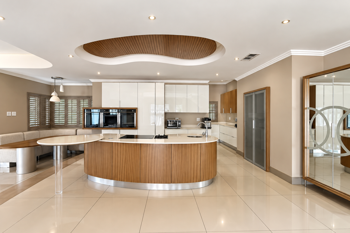 Modern kitchen featuring a curved island with integrated cooktop, high-gloss cabinetry, built-in ovens, and a unique recessed ceiling design with ambient lighting.