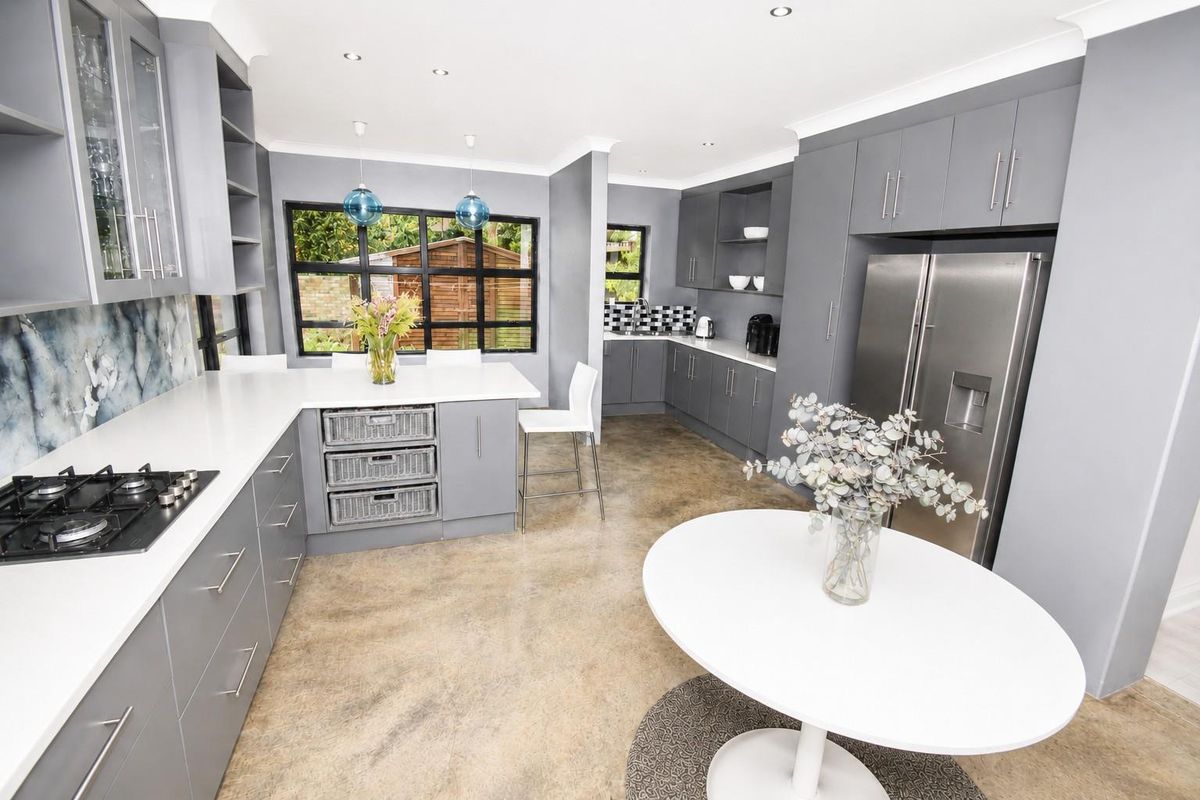 Modern kitchen featuring grey cabinetry, white stone countertops, a built-in gas hob, and polished concrete flooring with an open-plan layout.