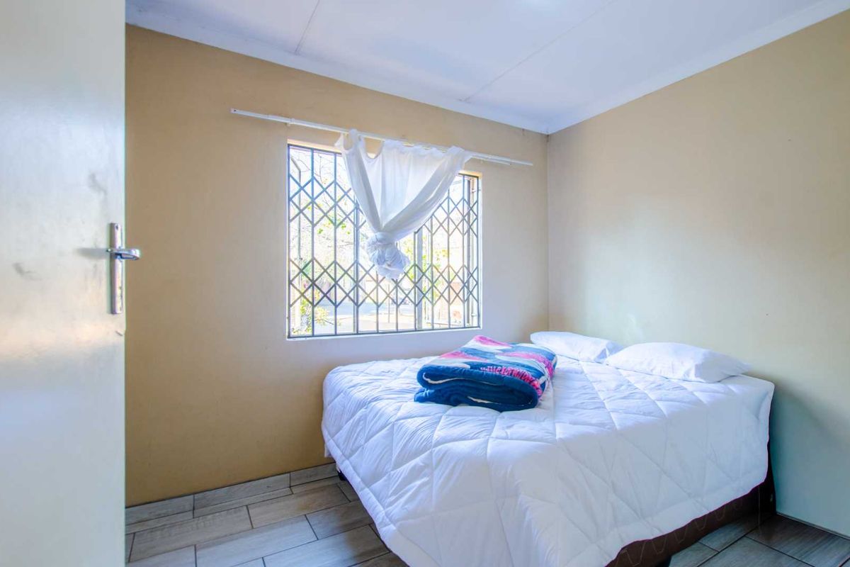 A functional bedroom featuring tiled flooring, a window with security bars, and neutral wall tones, providing a simple and practical living space.