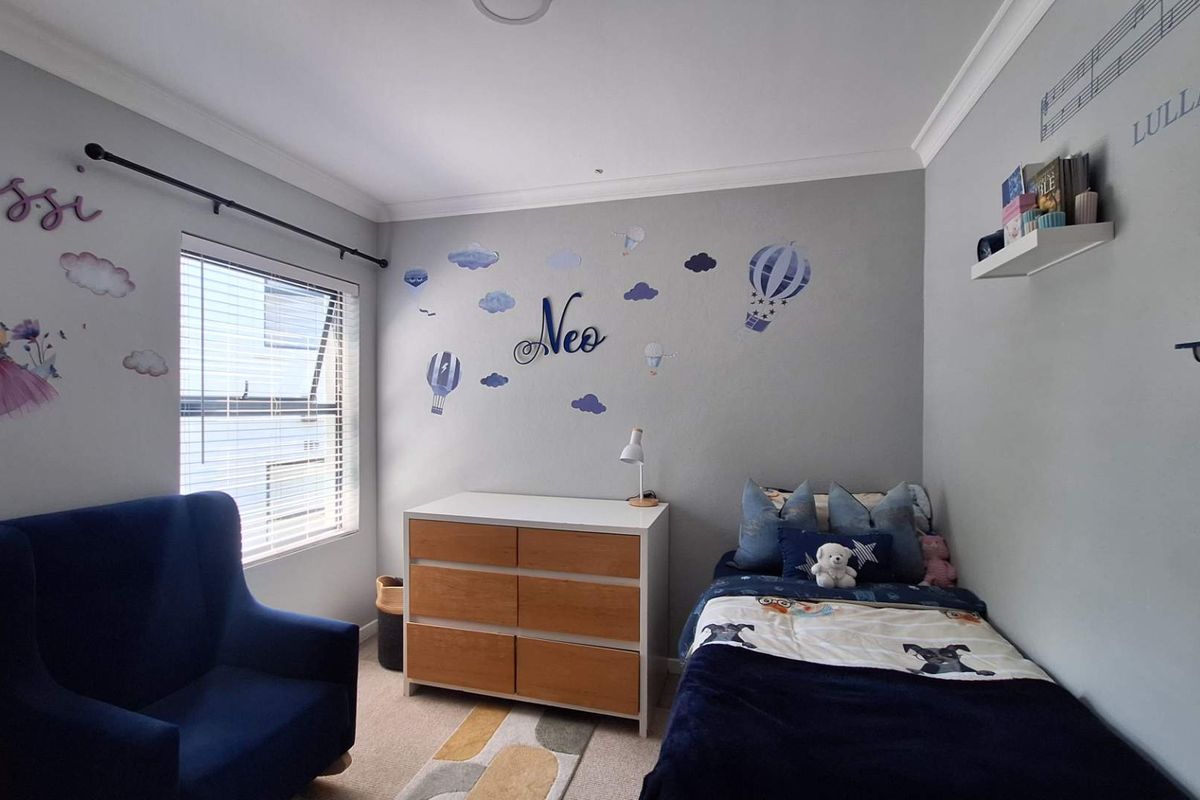 A well-maintained bedroom featuring neutral grey walls, carpeted flooring, and a window with fitted blinds.