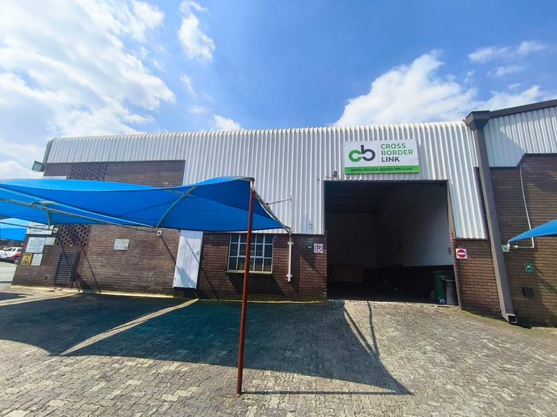 Front exterior view of an industrial warehouse facility featuring a large roller door entrance, brick and corrugated metal facade, and paved parking area.
