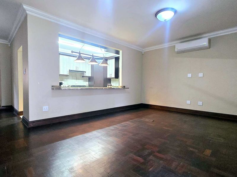 Spacious open-plan living area featuring dark parquet flooring, a granite breakfast bar pass-through to the kitchen, and a wall-mounted air conditioning unit.