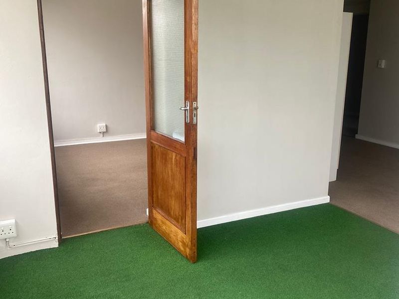 An empty living area featuring a timber door with a frosted glass panel and green carpeting, offering a blank canvas for renovation.