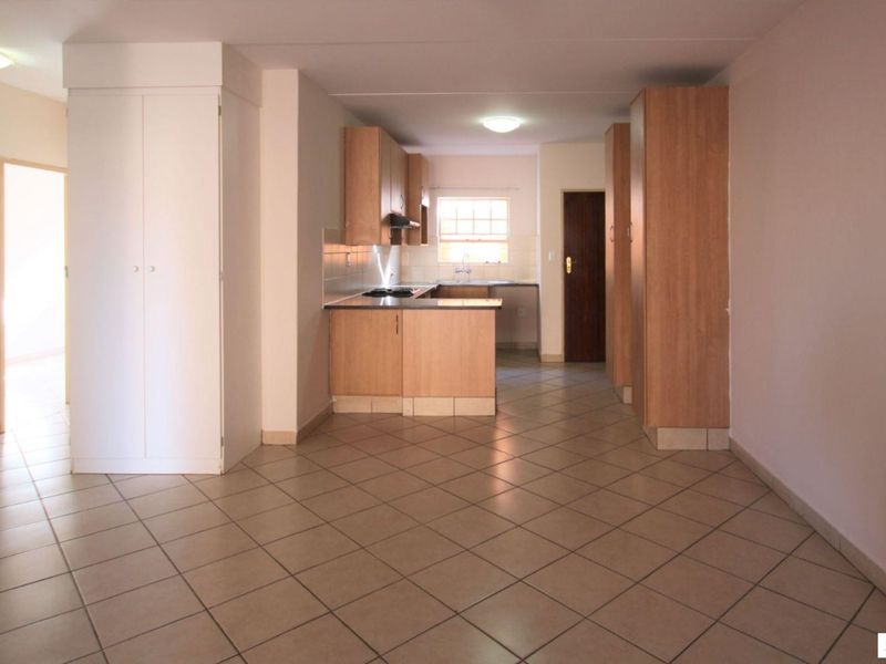 An open-plan living and kitchen area featuring tiled flooring, built-in wooden cabinetry, and a functional kitchen layout with a hob and extractor fan.