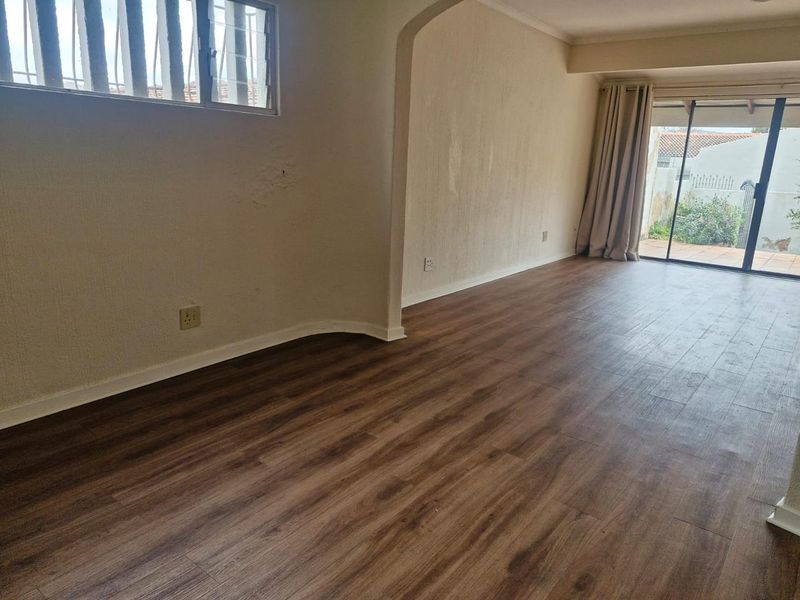 An empty living room featuring wood-look laminate flooring, an arched transition, and sliding glass doors leading to an outdoor patio area.