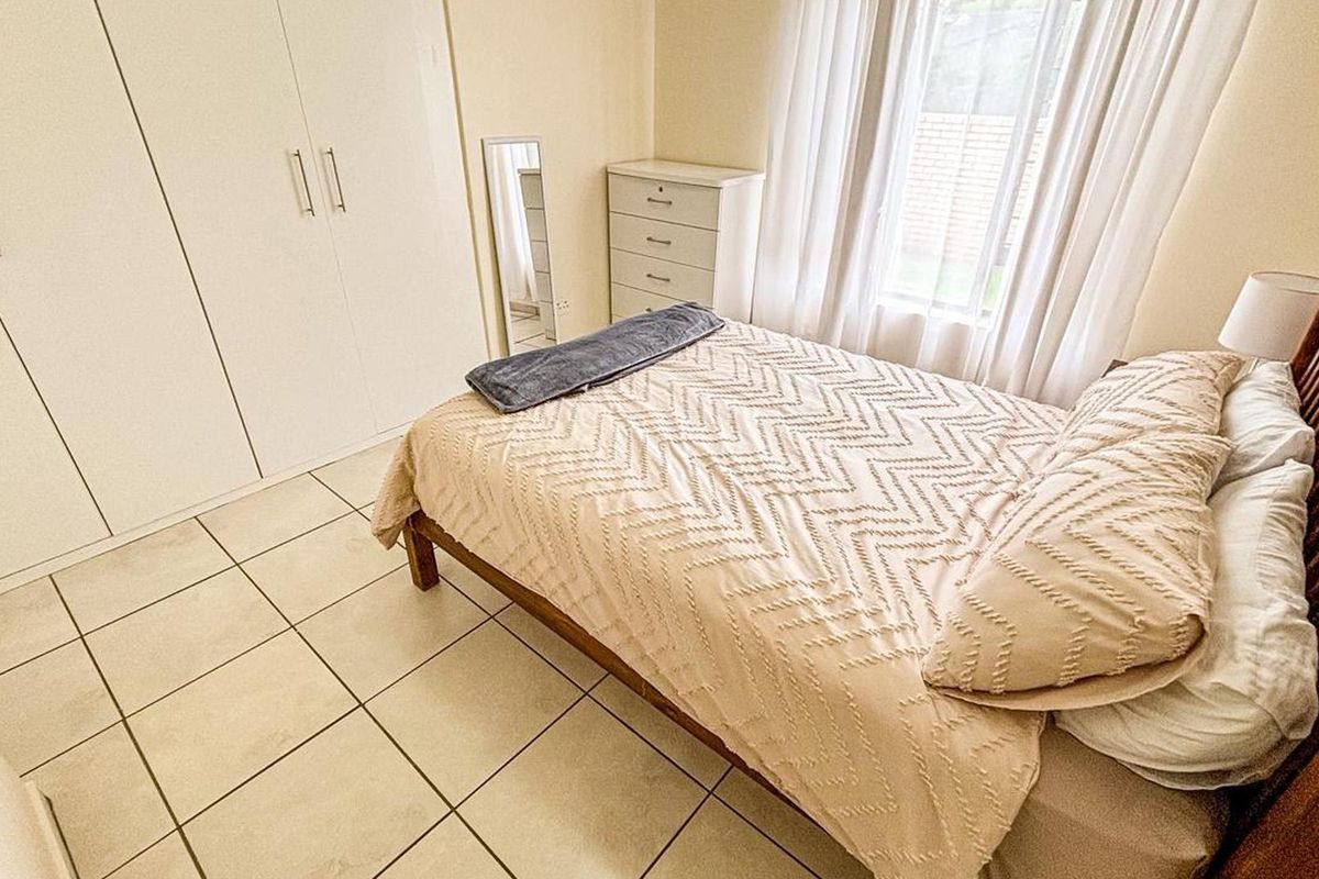 A well-maintained bedroom featuring neutral tiled flooring and ample built-in cupboard storage, offering a clean and functional living space.