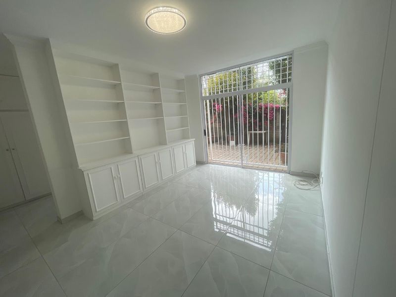 A bright, empty living room featuring polished tiled floors, extensive built-in cabinetry with shelving, and a sliding glass door leading to a private patio.