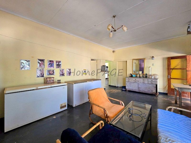 A spacious living area featuring high ceilings and original flooring, requiring cosmetic updates to modernize the interior finishes.
