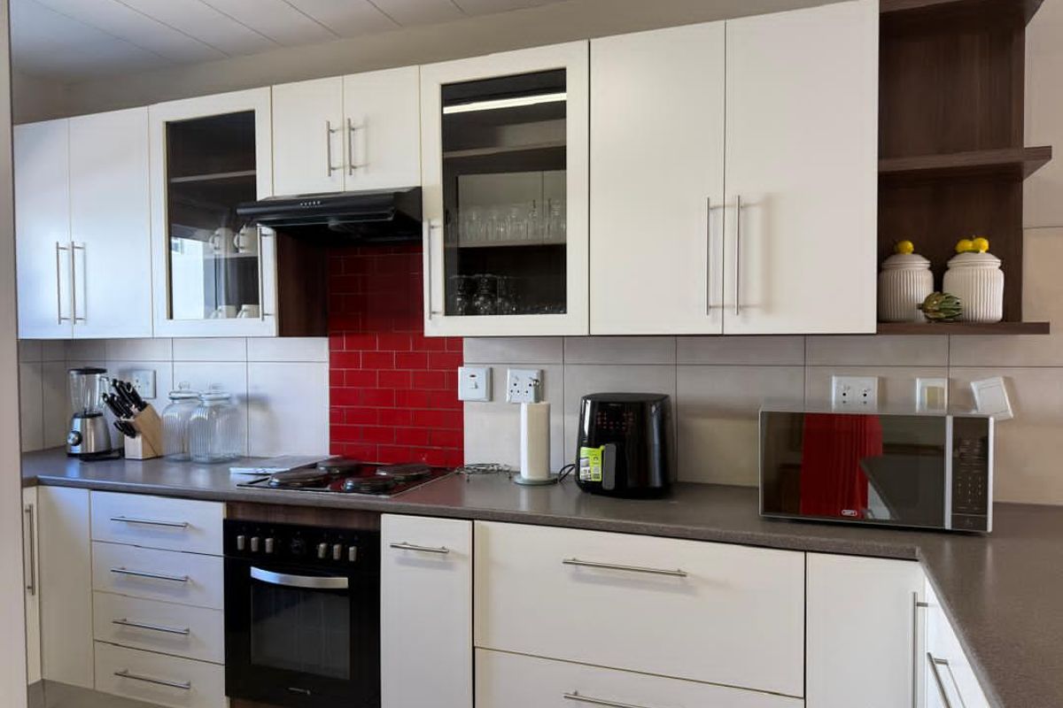 A modern kitchen featuring white cabinetry, contrasting dark countertops, a red tiled splashback, and a built-in oven with an extractor fan.
