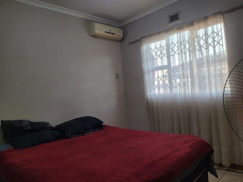 A bedroom featuring a wall-mounted air conditioning unit and a window fitted with a security gate.