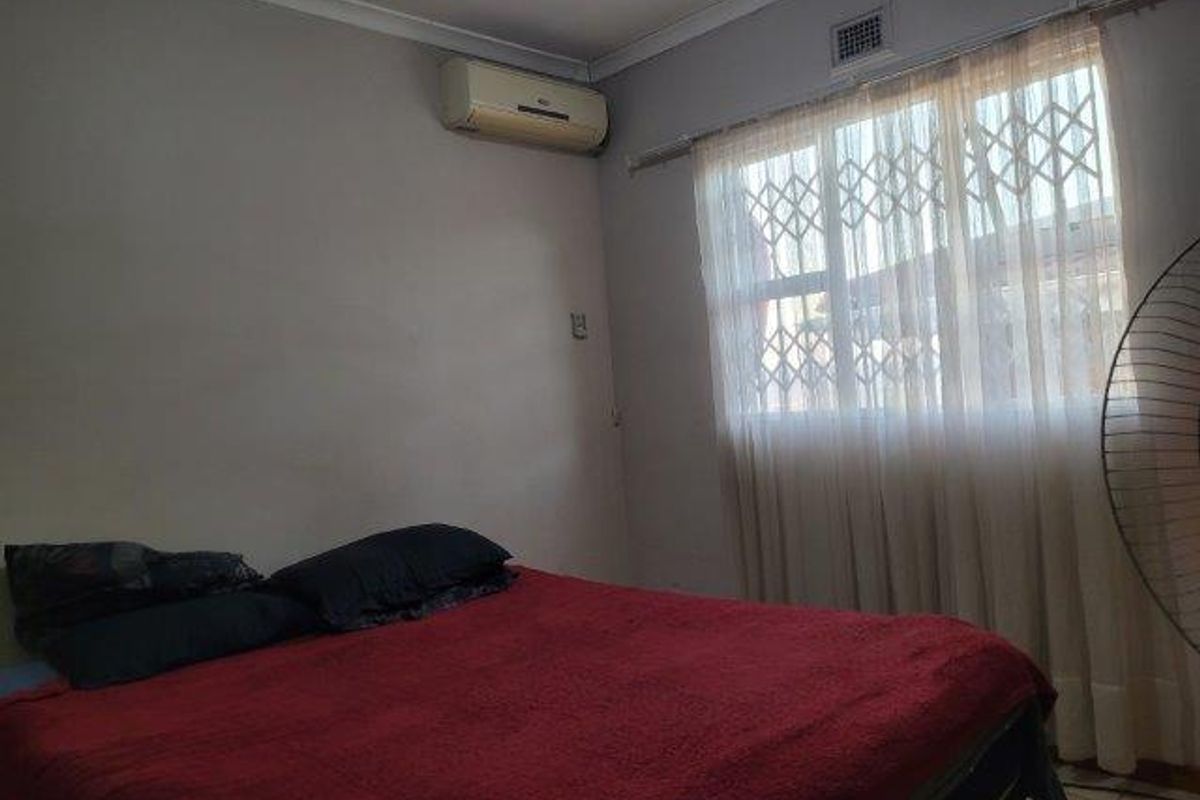 A bedroom featuring a wall-mounted air conditioning unit and a window fitted with a security gate.