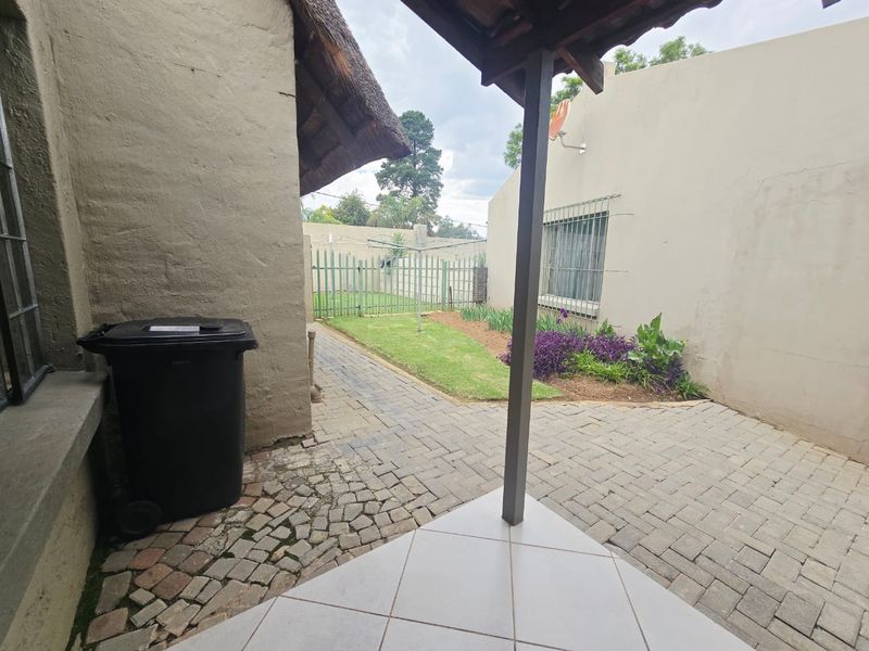 A covered patio area with paved flooring, overlooking a small private garden with a metal fence and security-barred windows.