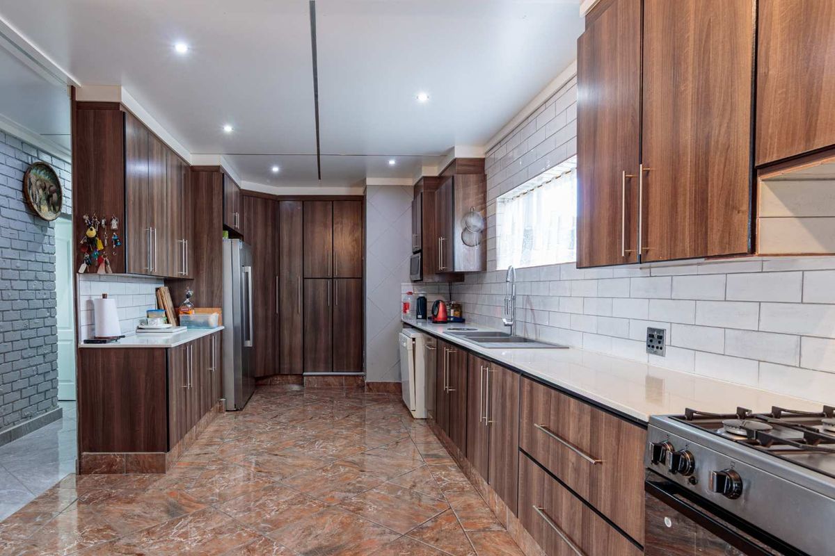 Modern kitchen featuring wood-grain cabinetry, stone countertops, subway tile backsplash, and a stainless steel gas stove with ample storage space.
