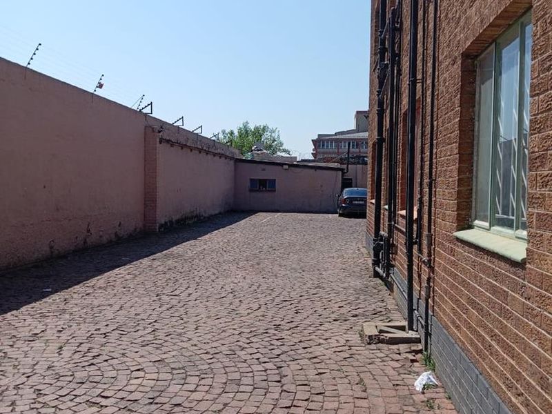 Rear exterior area featuring cobblestone paving, brick building facade, and perimeter wall with electric fencing.