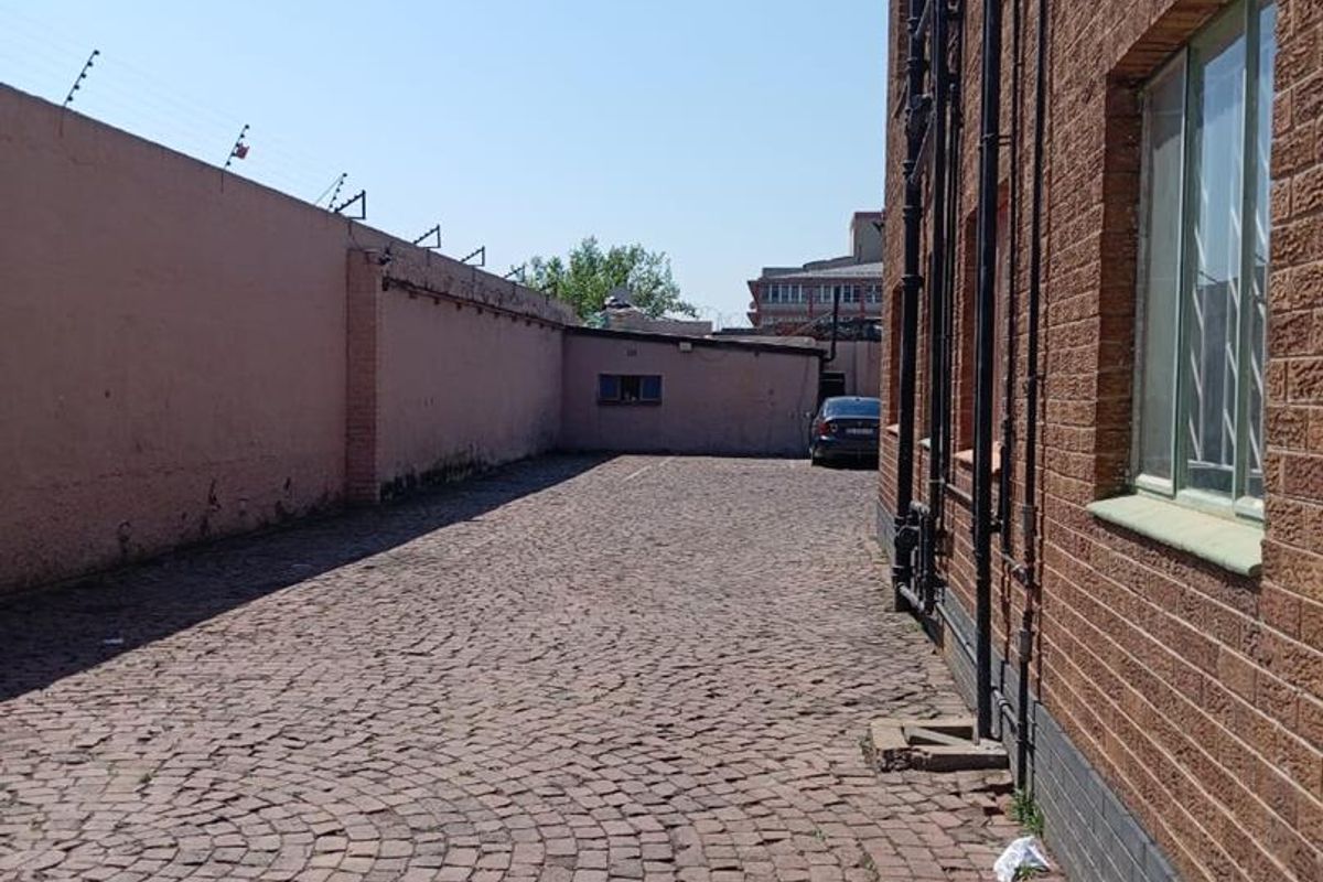 Rear exterior area featuring cobblestone paving, brick building facade, and perimeter wall with electric fencing.