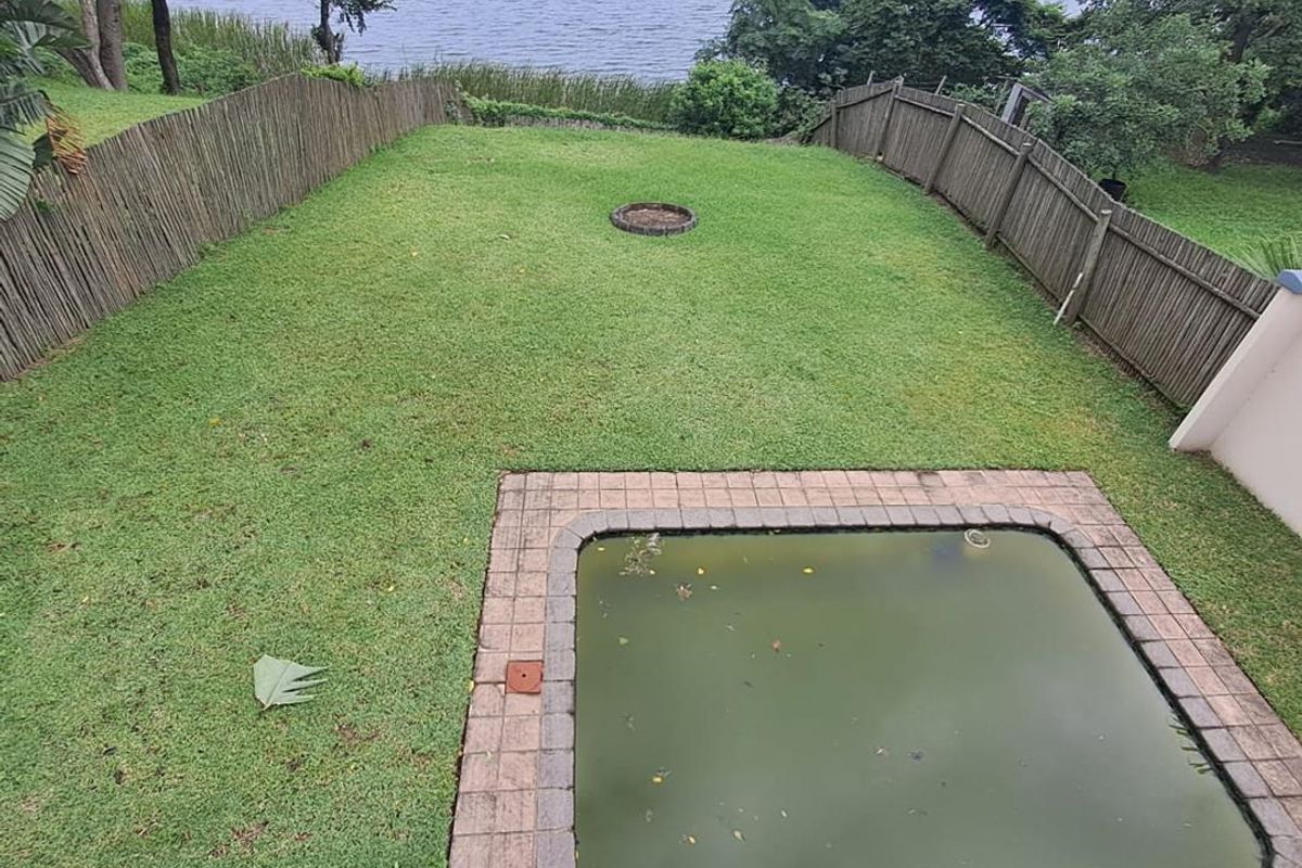A rear garden featuring a lawn, a small pool requiring maintenance, and timber fencing, overlooking a large body of water.