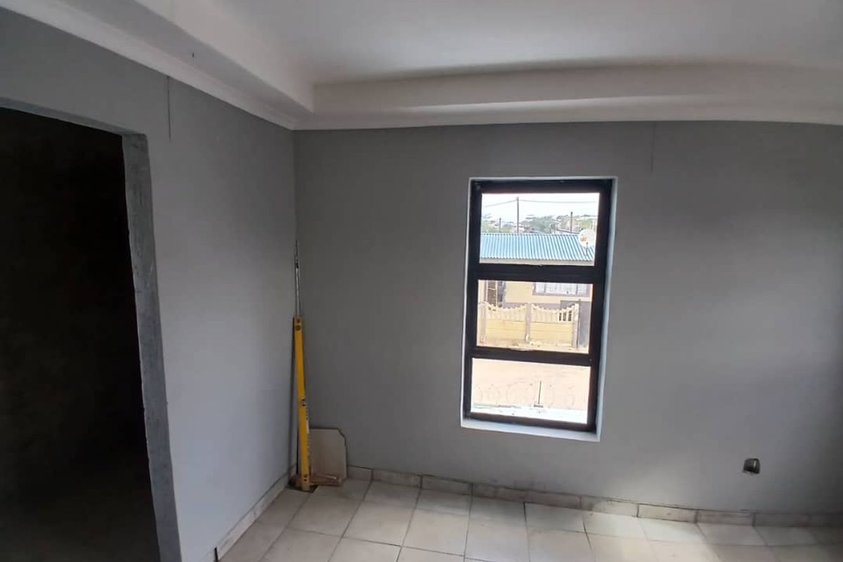 An empty bedroom featuring tiled flooring, a black aluminium window frame, and coved ceiling, currently in a basic, unfinished state.