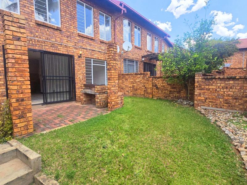 Rear exterior view of a townhouse featuring a face brick facade, a private garden with lawn, and a built-in brick braai area.