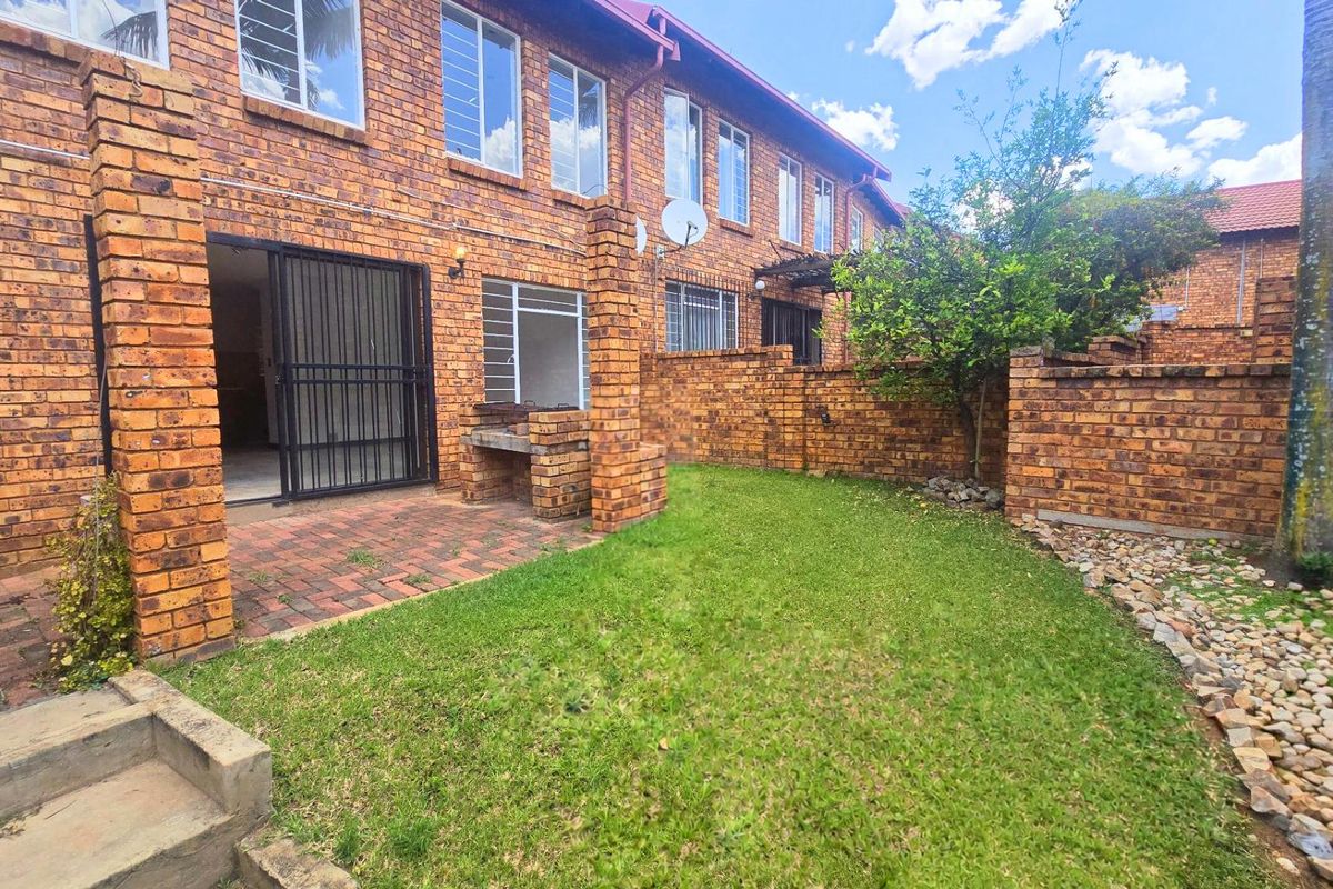 Rear exterior view of a townhouse featuring a face brick facade, a private garden with lawn, and a built-in brick braai area.