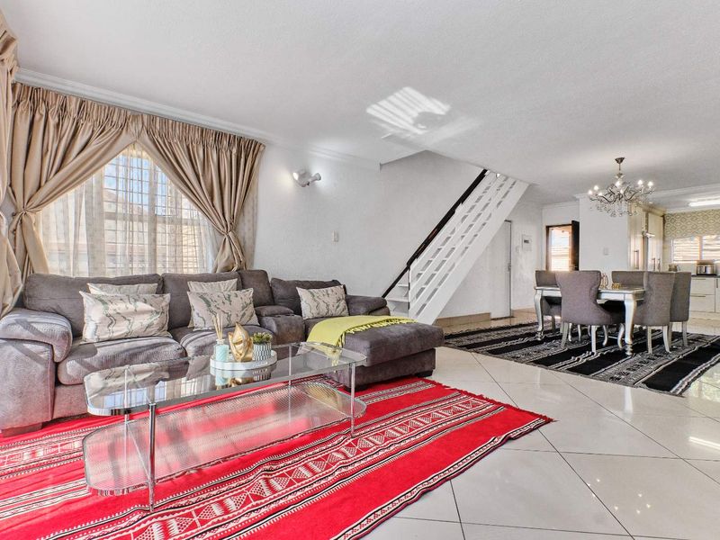 Spacious open-plan living and dining area featuring tiled floors, a staircase, and a modern kitchen visible in the background.