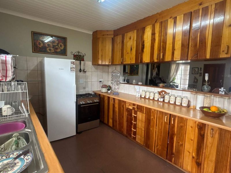A functional kitchen featuring extensive wooden cabinetry, laminate countertops, a gas stove, and a double bowl stainless steel sink with tiled backsplash.