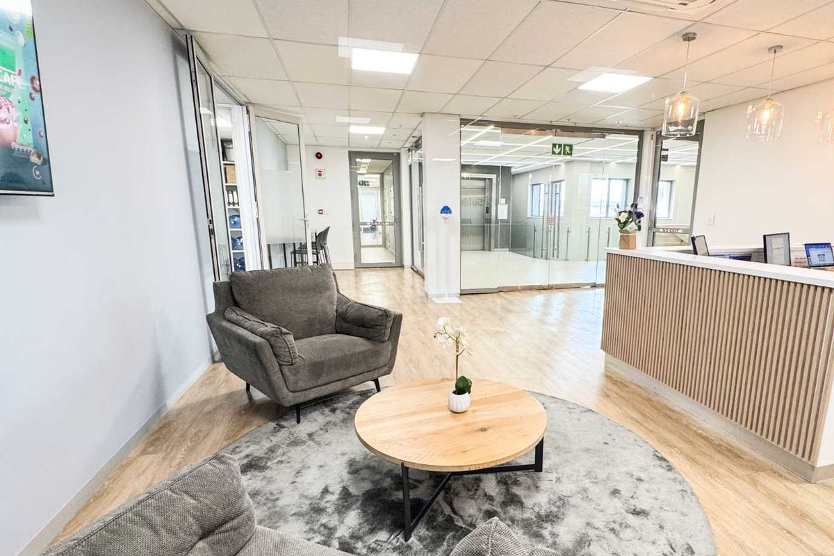 Modern office reception area featuring a sleek reception desk, glass partitions, suspended ceiling with recessed lighting, and light wood-look laminate flooring.
