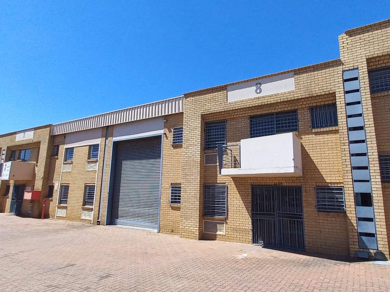 Exterior view of a multi-unit industrial complex featuring brick facades, roller shutter doors, and paved driveway access.
