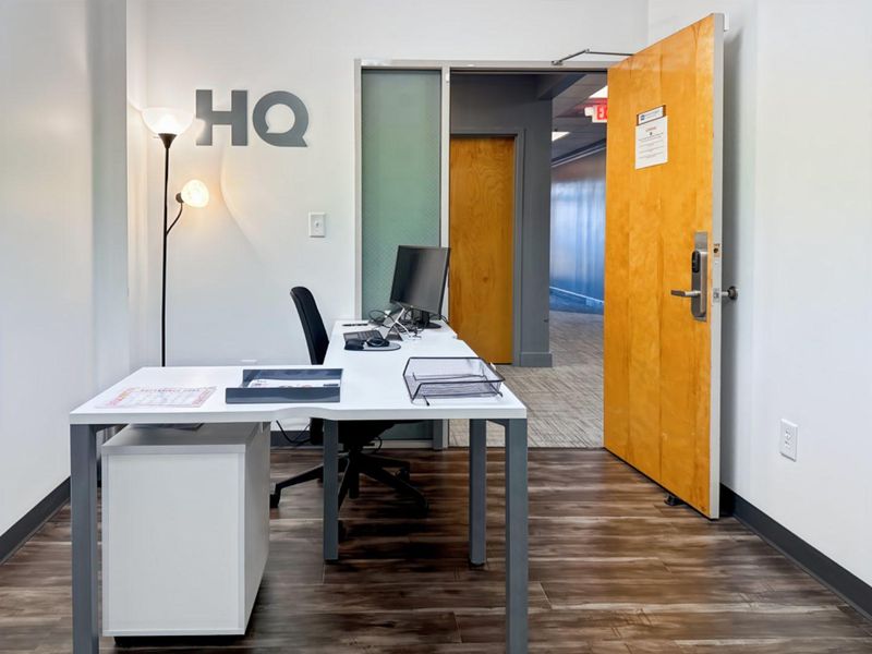 A professional office space featuring wood-look flooring, a solid wood door with electronic access control, and a frosted glass sidelight for natural light.