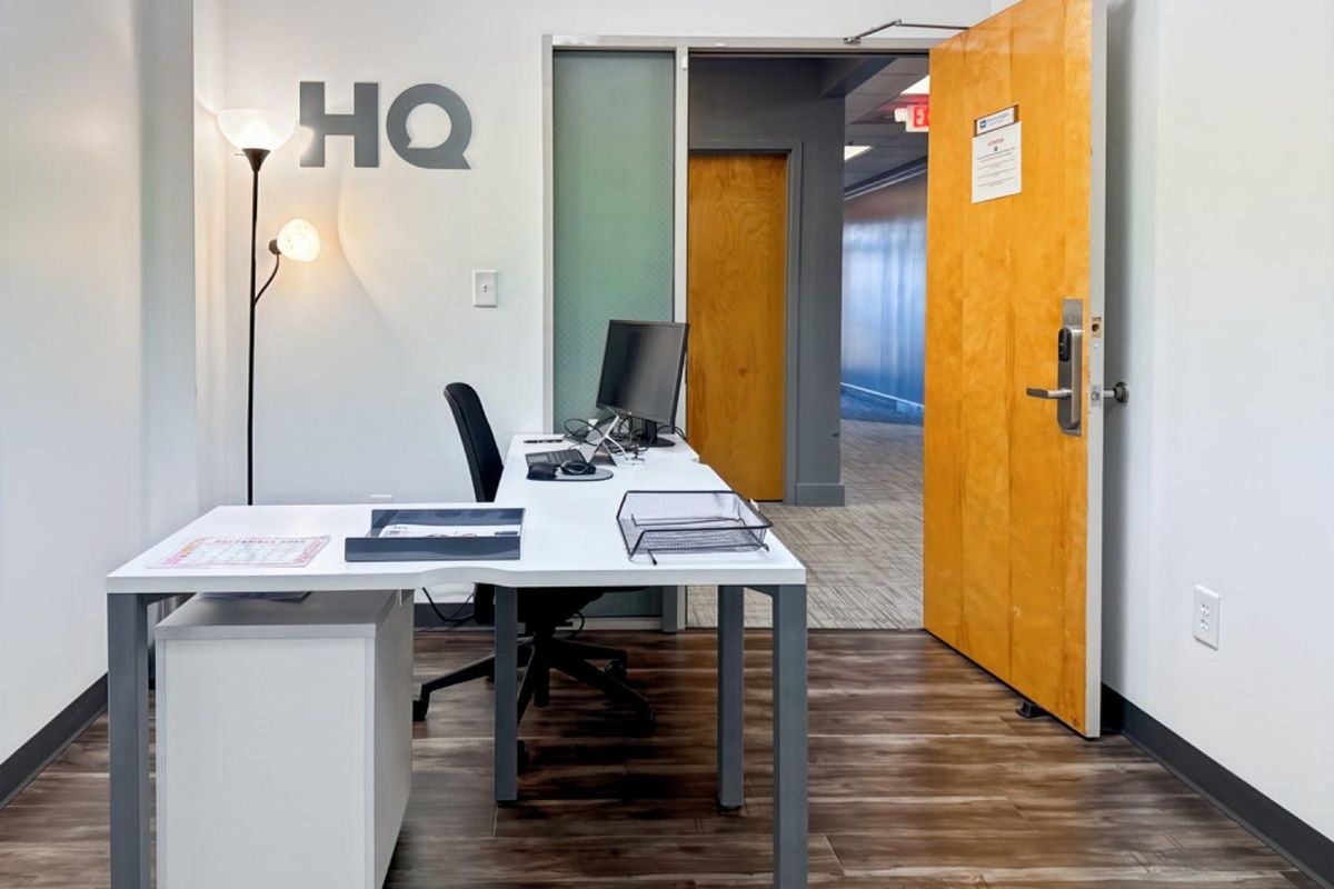 A professional office space featuring wood-look flooring, a solid wood door with electronic access control, and a frosted glass sidelight for natural light.