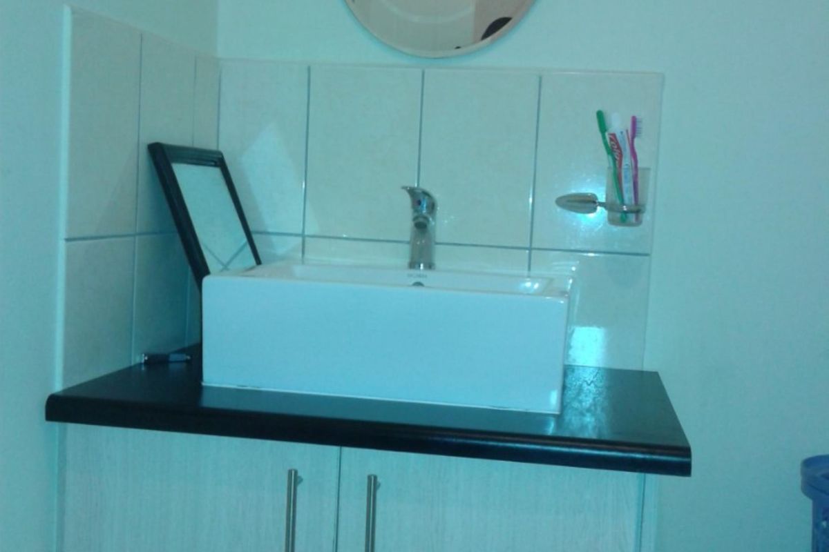 A bathroom vanity featuring a modern vessel sink, dark countertop, and light wood-finish cabinetry with a wall-mounted mirror and tiled splashback.