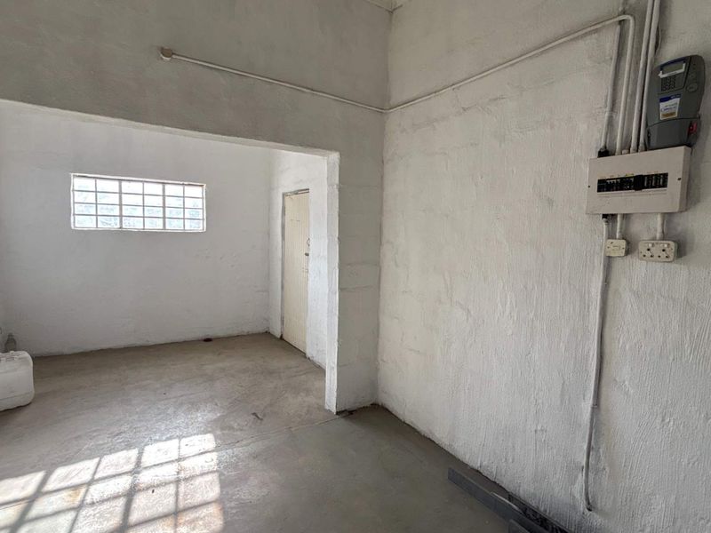 An empty industrial utility space featuring exposed electrical infrastructure, concrete flooring, and a grid window, suitable for storage or workshop use.