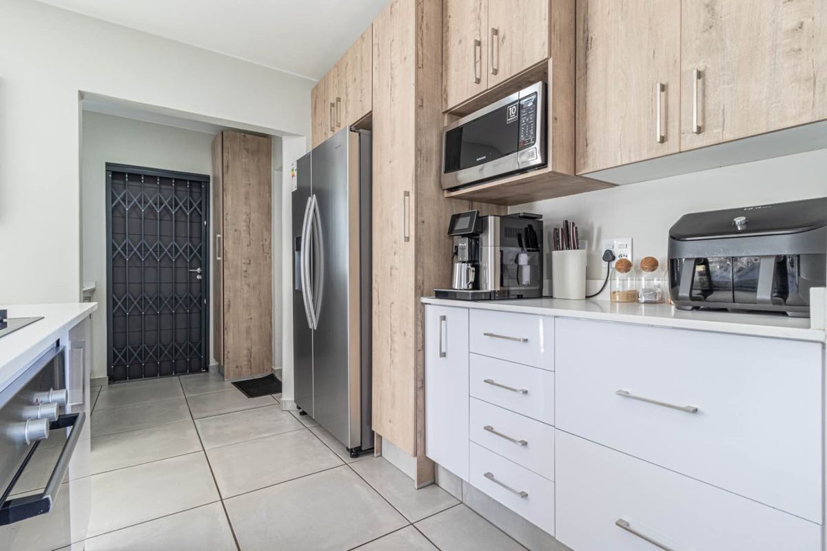 Modern kitchen featuring light wood-grain cabinetry, white high-gloss drawers, stone countertops, and a built-in microwave, leading to a secure entrance door.