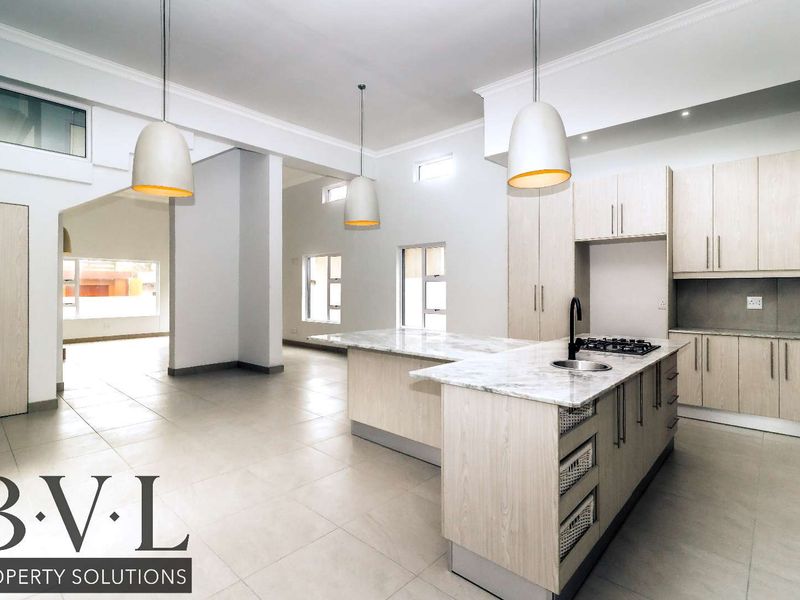 Spacious open-plan kitchen featuring modern light wood cabinetry, stone countertops, a central island with a gas hob, and elegant pendant lighting.