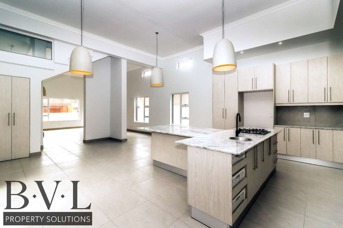 Spacious open-plan kitchen featuring modern light wood cabinetry, stone countertops, a central island with a gas hob, and elegant pendant lighting.