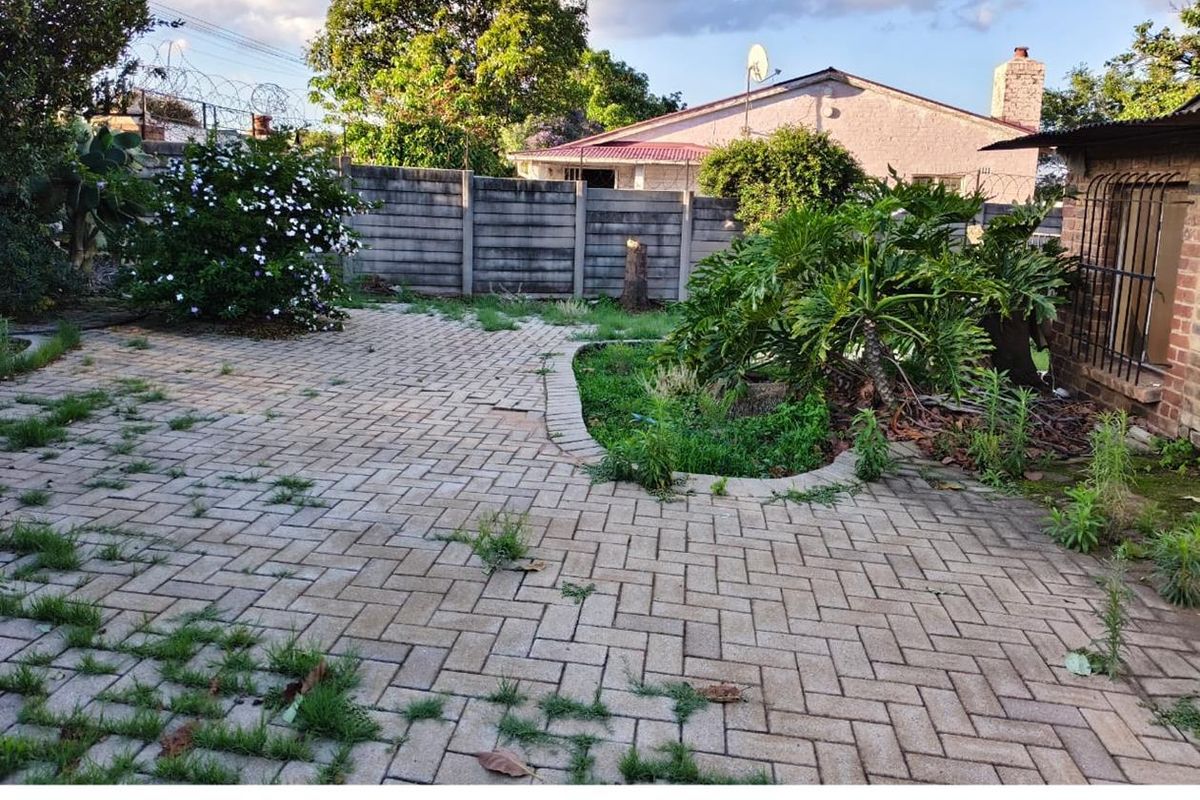 A rear garden area featuring paved patio space, established garden beds, and a perimeter boundary wall.
