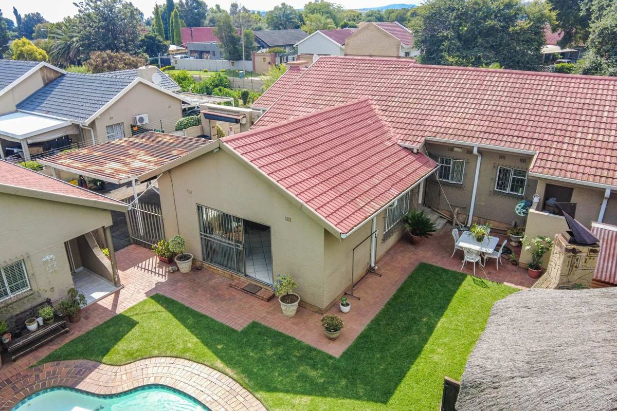 Aerial view of the property featuring a tiled roof, swimming pool, paved patio area, and a carport with a rear garden.