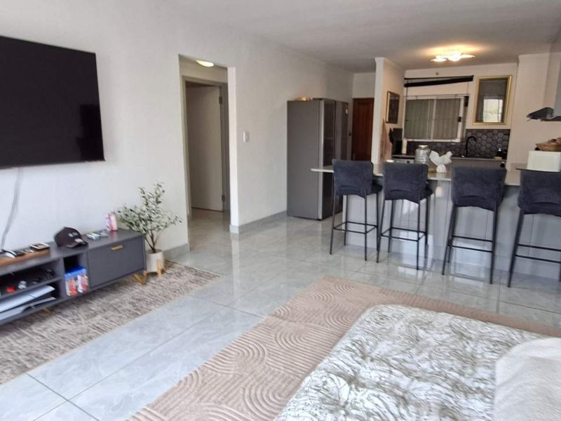An open-plan living and kitchen area featuring tiled flooring, a breakfast bar, and modern kitchen cabinetry.