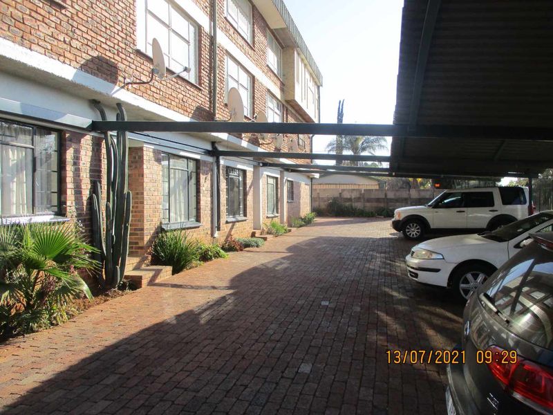 Exterior view of an apartment complex featuring a paved driveway and covered carport parking area with brick building facade.