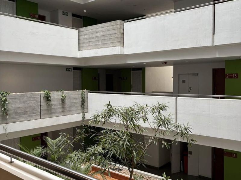A modern apartment complex atrium featuring multi-level walkways, concrete balustrades, and a central landscaped courtyard area.