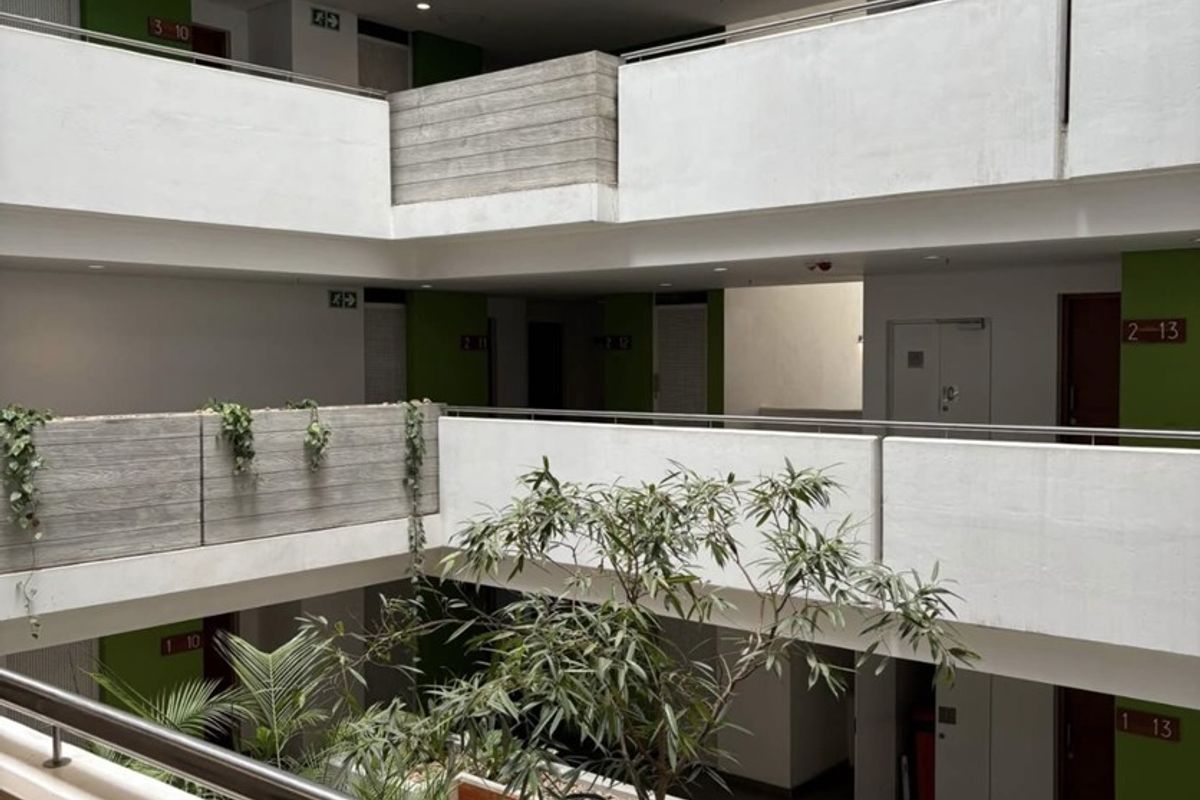 A modern apartment complex atrium featuring multi-level walkways, concrete balustrades, and a central landscaped courtyard area.
