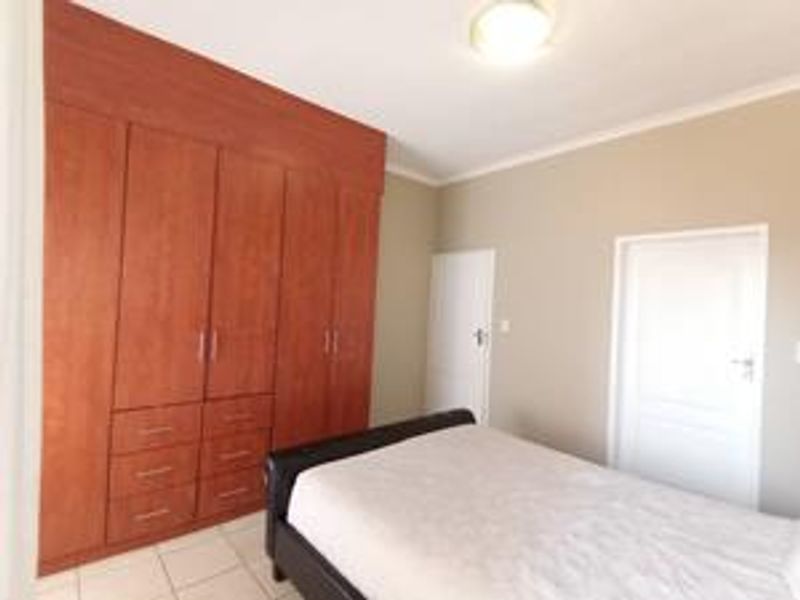 A bedroom featuring built-in wooden cupboards, tiled flooring, and neutral wall tones, providing a functional and clean living space.