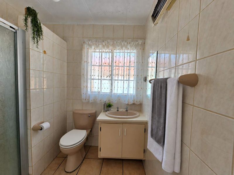 A functional bathroom featuring a shower enclosure, vanity basin, and toilet with neutral wall and floor tiling.