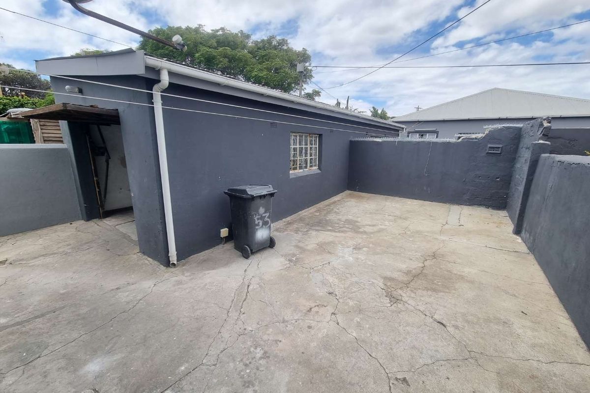 Rear exterior area featuring concrete paving and boundary walls, showing signs of wear and requiring maintenance.