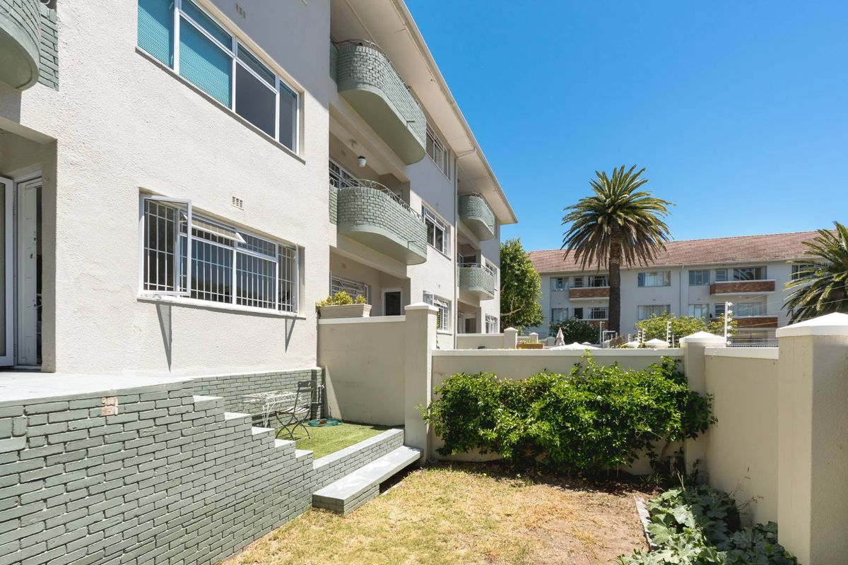 Rear view of the apartment building featuring a small private garden area, boundary wall, and upper-level balconies with security bars.