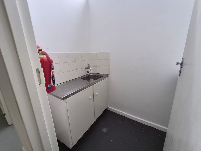 A compact utility space featuring a stainless steel sink, built-in cabinetry, and tiled splashback, suitable for storage or cleaning tasks.