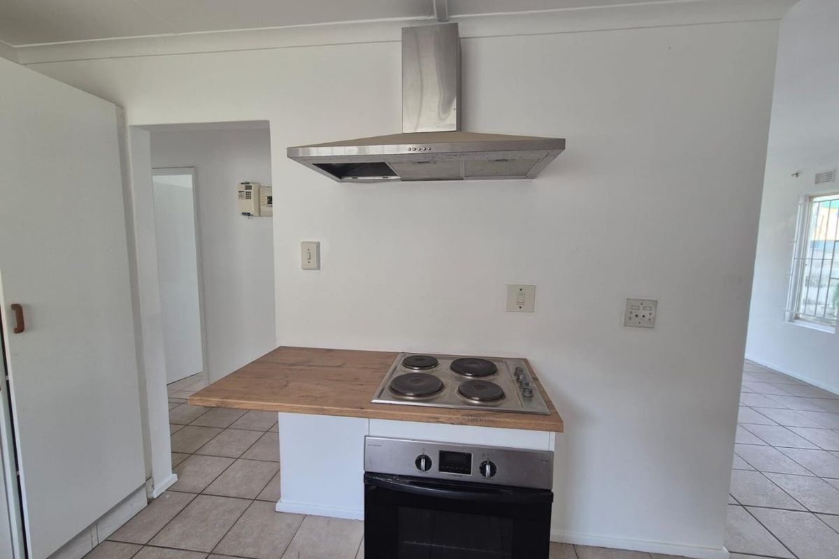 A functional kitchen area featuring a built-in oven, electric hob, stainless steel extractor fan, and tiled flooring.