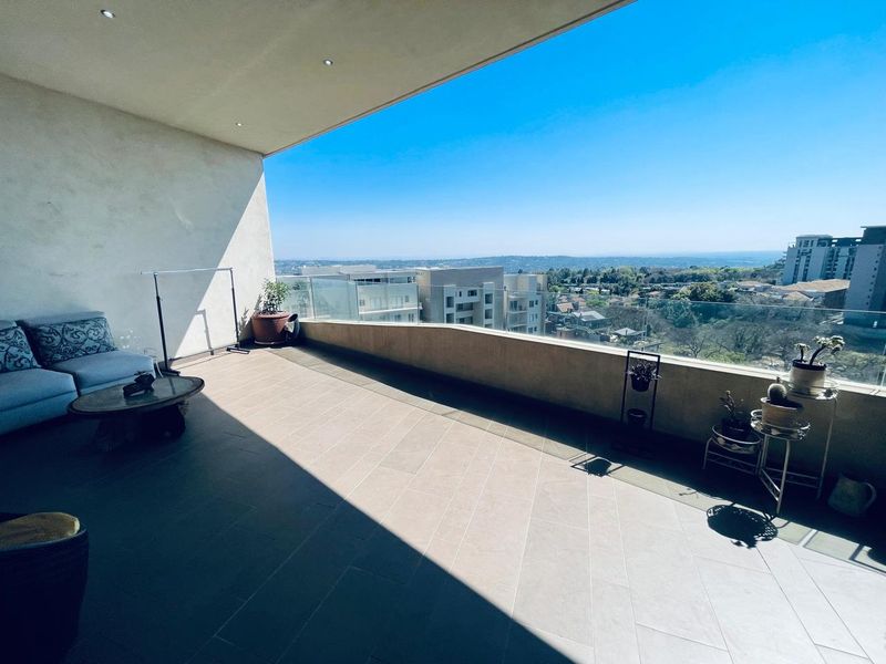 Spacious covered balcony featuring modern tiled flooring, recessed lighting, and a frameless glass balustrade offering expansive elevated views.
