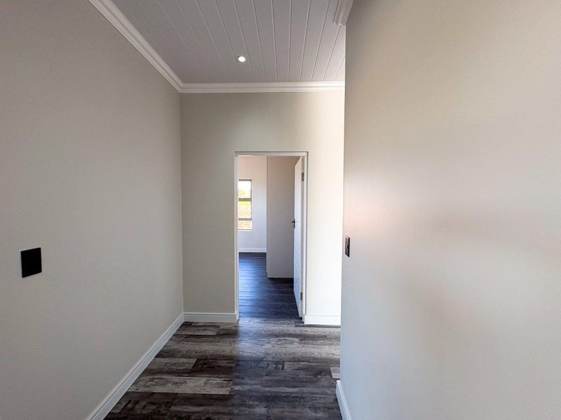 A clean, modern hallway featuring neutral walls, wood-look laminate flooring, and a white tongue and groove ceiling with recessed lighting.